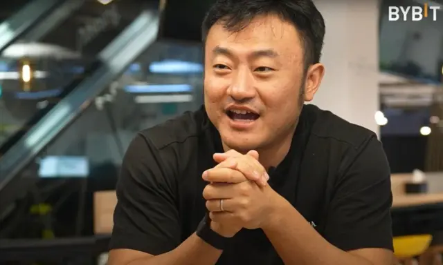 Ben Zhou, w czarnej koszulce, z dłońmi złożonymi na piersi, opowiada o przyszłości kryptowalut.