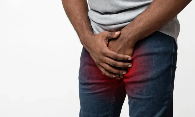 Mężczyzna trzyma się za krocze, gdzie widoczny jest czerwony obszar bólu, sugerujący ropień prostaty.