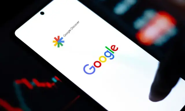 Ekran smartfona z logo Google i napisem Google Discover. W tle wykresy giełdowe.