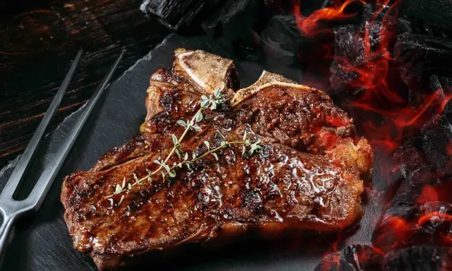 Un jugoso chuleton a la brasa, con romero fresco, listo para ser servido junto a brasas ardientes.
