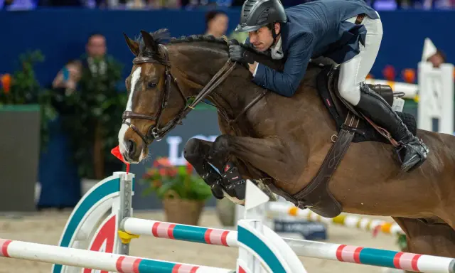 Reiter und Pferd im Sprung über ein Hindernis. Die Haltung des Reiters, die Anspannung des Pferdes und die elektrischen Sporen deuten auf einen spannenden Wettkampf hin.