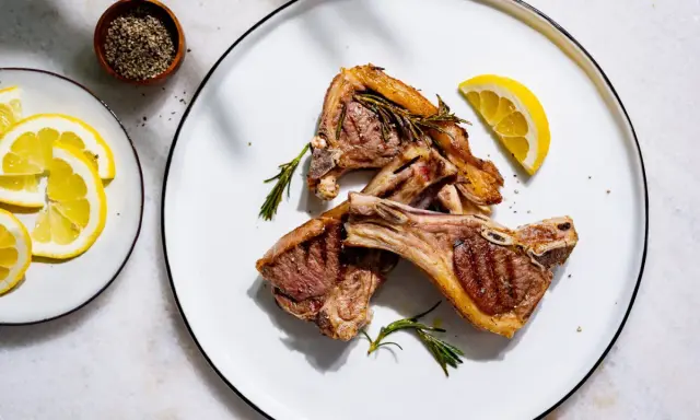 Côtelettes d'agneau grillées, parfumées à la marinade, garnies de romarin frais et de quartiers de citron.
