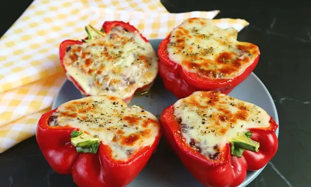 Quattro peperoni ripieni in friggitrice ad aria, con formaggio fuso e spezie, pronti per essere gustati.