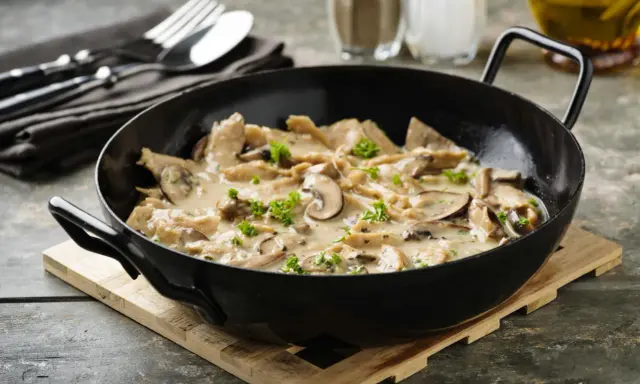 Herzhaftes geschnetzeltes mit Pilzen in cremiger Sauce, garniert mit Petersilie, serviert in einer schwarzen Pfanne.