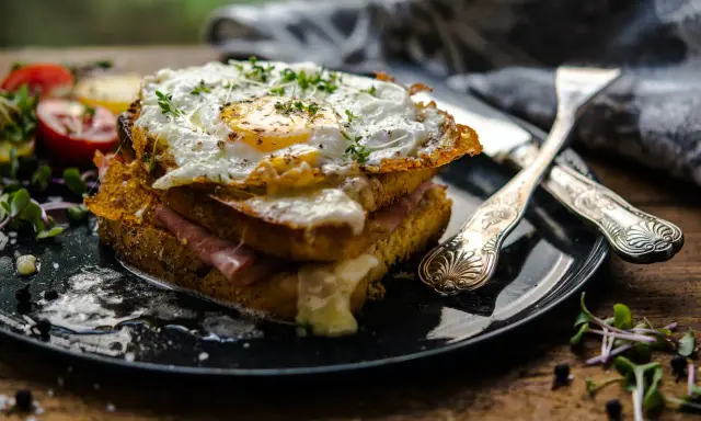 Un croque-madame gourmand, un des plats typiques parisiens, avec un œuf au plat, jambon et fromage fondant, servi avec des tomates et des pousses.
