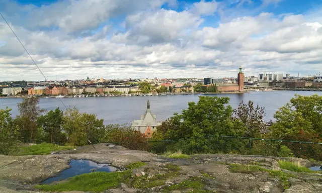 Vy över Riddarfjärden från Skinnarviksberget Stockholm, med Stadshuset i bakgrunden under en molnig himmel.