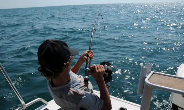 Ragazzo con cappellino nero pesca in mare, mostrando alcuni metodi di pesca con la canna.