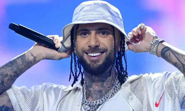 Malik Montana we Wrocławiu, w białym bucket hat, z mikrofonem w dłoni, uśmiecha się do fanów.