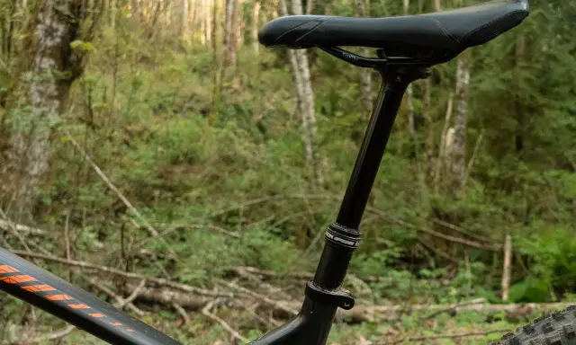 Regulowany **dropper rower** w lesie. Czarny amortyzowany wspornik siodła z siodełkiem na tle zieleni.