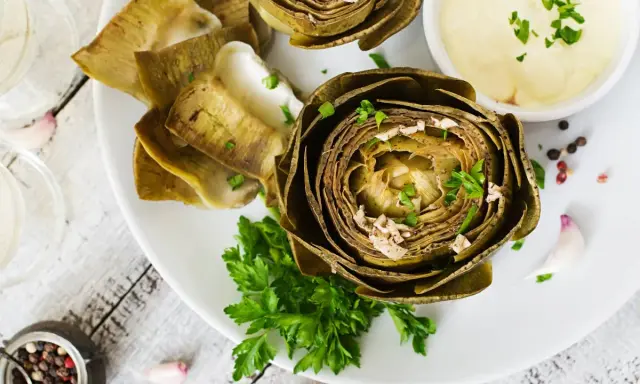 Deliciosas alcachofas al horno, tiernas y doradas, servidas con una cremosa salsa y perejil fresco. Un plato perfecto para disfrutar.