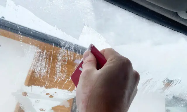 Dłoń zeskrobuje szron na szybie, odsłaniając fragmenty drewnianej elewacji. Zima daje się we znaki.