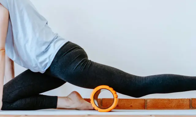 Frau in Sportkleidung dehnt sich mit einem Faszienroller.