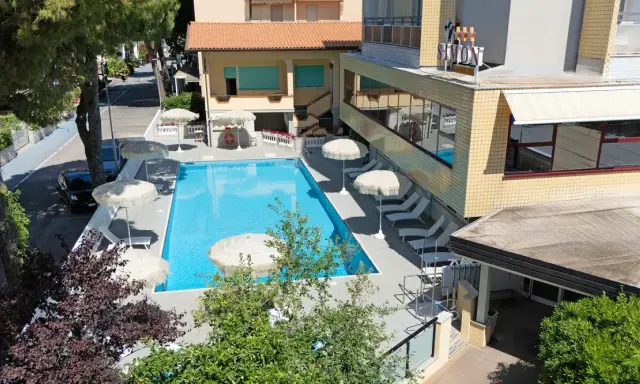 Piscina invitante e lettini prendisole al **hotel Simon Gatteo Mare**. Ombrelloni bianchi e vegetazione rigogliosa creano un'oasi di relax.
