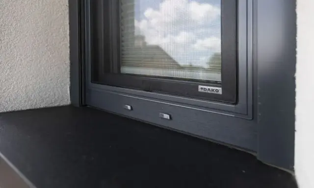 Szary parapet zewnętrzny pod oknem z moskitierą. Zastanawiasz się, czym przykleić parapet zewnętrzny blaszany?