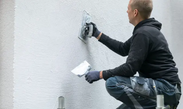 Artisan appliquant un enduit gratté sur un mur extérieur.