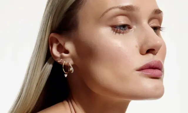 Delikatne kolczyki z kwiatami i serduszkiem, zdobiące ucho modelki, dodają subtelnego blasku.