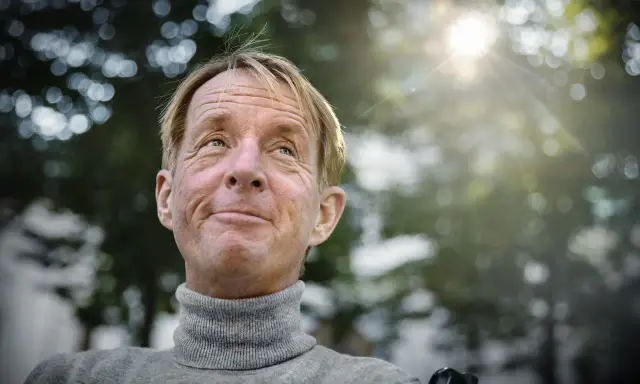 En leende man med rullstol, kanske en scen från filmer med Nils Hallberg, tittar upp mot solen.