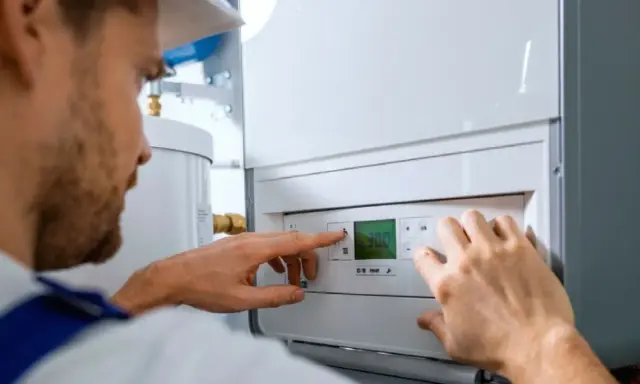 Técnico ajustando la temperatura en un calentador de gas butano. La pantalla digital muestra 30.0 grados.