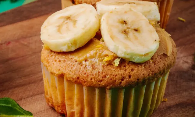 Pyszne muffinki bananowe fit z masłem orzechowym i plasterkami banana na drewnianej desce.