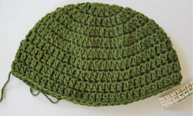 Gorro de lana verde tejido a mano, ideal para aprender como tejer un gorro de lana para principiantes. Cinta métrica al lado.