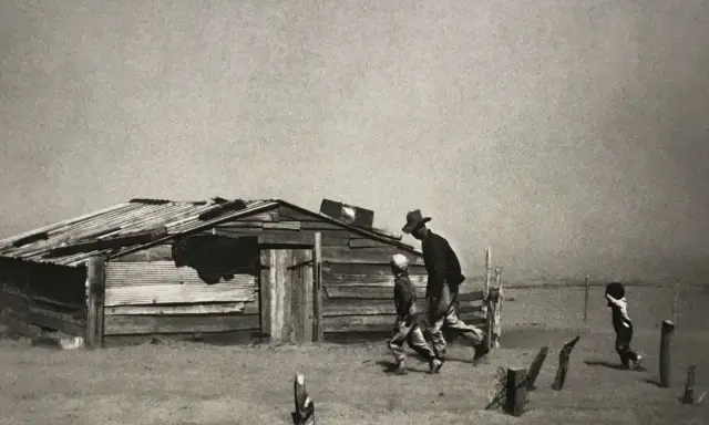 Dust Bowl migrants walk past a dilapidated shack in this iconic Arthur Rothstein photo, a stark reminder of hardship.