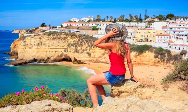 Kobieta w kapeluszu podziwia malownicze portugalia wybrzeże algarve z białymi domkami i turkusową wodą.