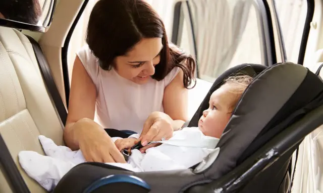 Madre abrochando el cinturón de seguridad a su bebé en la silla del coche. Los niños en el coche viajan seguros.