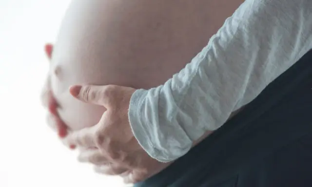 Dłonie obejmujące ciążowy brzuch, odczuwając ucisk na pęcherz w ciąży w II trymestrze.