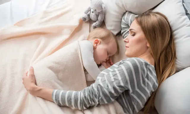 Mamma e bimbo dormono abbracciati, un tenero momento di co sleeping con un orsetto di peluche.
