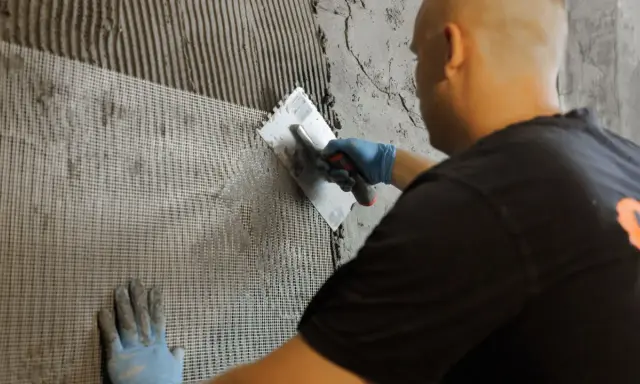 Mann verputzt Wand mit Armierungsgewebe. Perfekt für den Ausbau des Kellers.