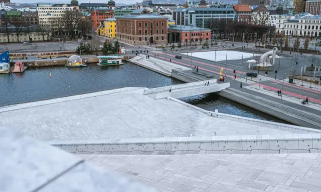 Widok z punktu widokowego Oslo na nowoczesną architekturę, wodę i plac z rzeźbą.