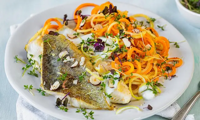 Gebratenes Fischfilet mit Spiralnudeln aus Karotten und Zucchini, garniert mit Kräutern und Mandelsplittern. Perfekt für leichte fasten rezepte.