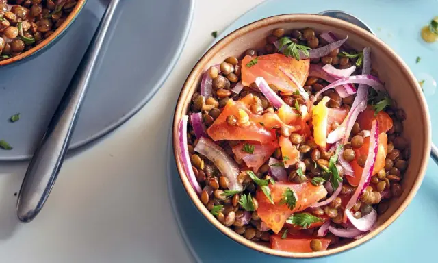 Salade de lentilles savoureuse avec des morceaux de saumon, des oignons rouges et du persil frais. Un plat coloré et nutritif.