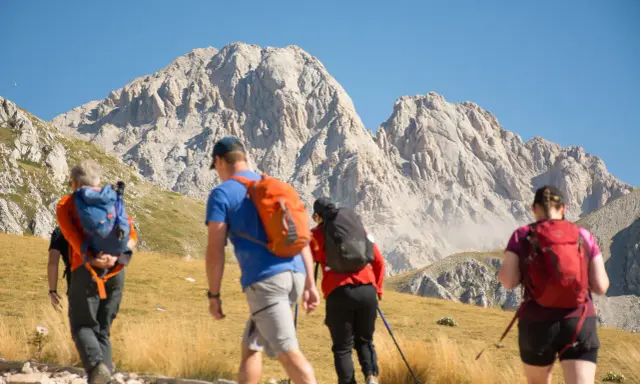 Escursionisti si dirigono verso un imponente corno grande, con zaini colorati e bastoncini da trekking.