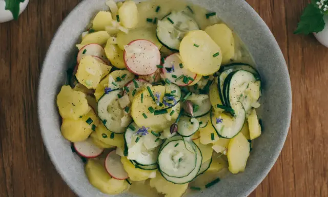 Kartoffelsalat mit Schale, garniert mit Radieschen, Gurken und Schnittlauch. Ein herzhaftes Gericht, das an Omas Küche erinnert.