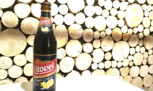 Butelka piwa Litovel Černý Citron na tle drewnianej ściany z plastrów drewna.