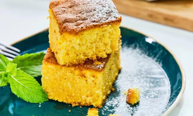 Dos porciones de bizcocho de calabaza espolvoreadas con azúcar glas, acompañadas de hojas de menta fresca en un plato azul.