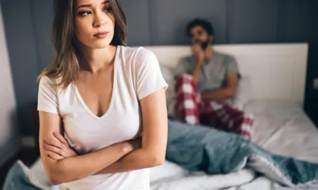 Kobieta zmartwiona, mężczyzna w tle. Problemy intymne, może uczulenie na spermę?