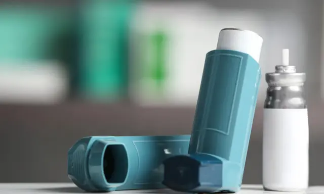 Zwei Inhalatoren, einer davon ein Symbicort-Spray, liegen auf einer weißen Oberfläche.