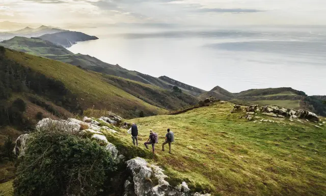 Trzech turystów podczas trekkingu na zielonym wzgórzu z widokiem na morze i góry.