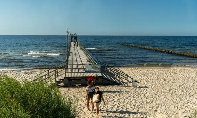 Sianożęty atrakcje: drewniane molo wchodzi w morze, plaża i fale.