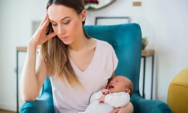 Zmęczona mama z płaczącym niemowlakiem na rękach, w fotelu, w poszukiwaniu siebie.