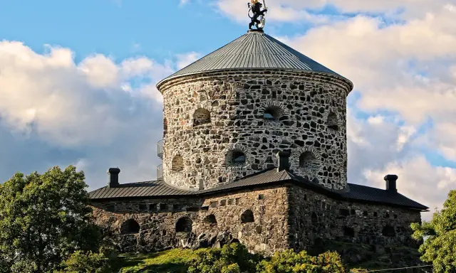 Skansen Lejonet, ett stendäckat torn med en gyllene lejonstaty på toppen, reser sig mot en molnig himmel.