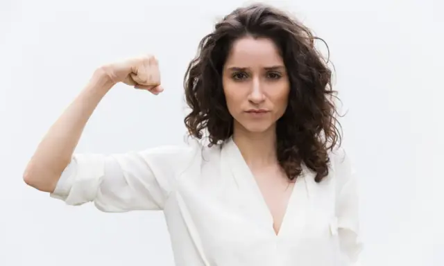 Kobieta pokazuje biceps, symbolizując siłę. Może to być metafora objawów wysokiego testosteronu, takich jak pewność siebie i determinacja.