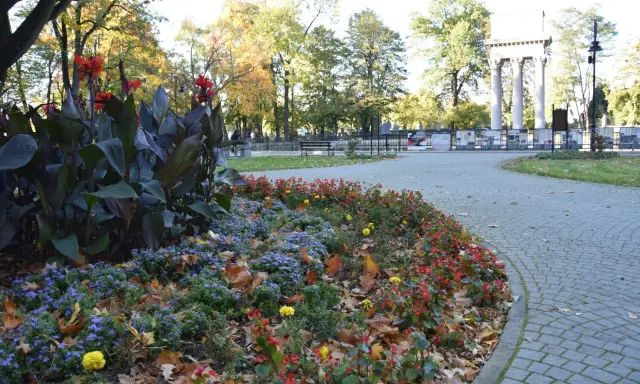 Jesienny park strzelecki Tarnów. Kolorowe rabaty kwiatowe i liście na brukowanej ścieżce.