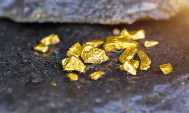 Pepite d'oro luccicanti su roccia umida. Scopri cosa significa oro 585, un metallo prezioso con una storia millenaria.
