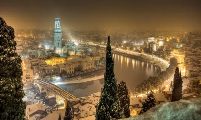 Verona innevata, un'incantevole **città da visitare a dicembre**. La neve copre i tetti e il fiume Adige riflette le luci della città.