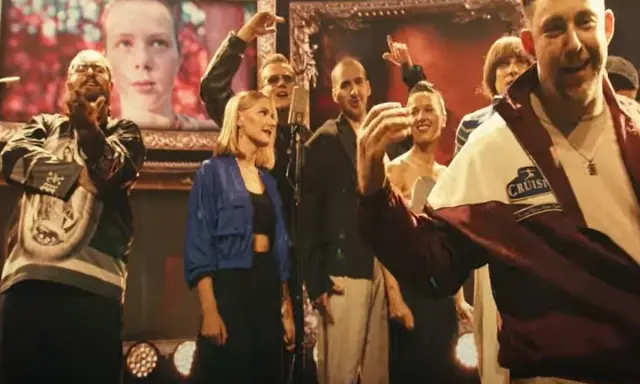 Witajcie w naszej bajce! Kto śpiewa? Grupa ludzi na scenie, z portretem w tle, w radosnym nastroju.