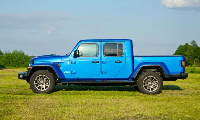 Niebieski Jeep Gladiator na tle zielonej łąki i drzew. Ten wszechstronny pickup jest gotowy na każdą przygodę.