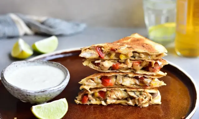 Stos **quesadilli z kurczakiem**, papryką i serem, podane z dipem i limonką.